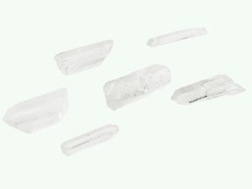 SKwarc srebrny - kamień naturalny, surowy, nieszlifowany. ześć białych kryształków na jasnym tle, ułożonych w różnych kierunkach.