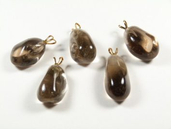 Pięć brązowych kamieni z zawieszkami leży na białym tle.