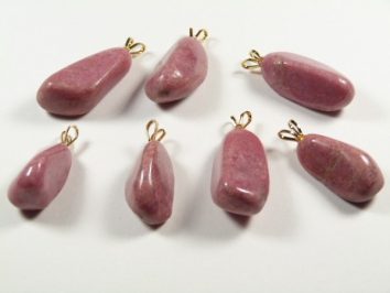 Siedem różowych kamieni z zawieszkami ułożonych na białym tle.