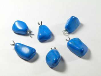Sześć niebieskich kamieni z zawieszkami leży na białym tle.