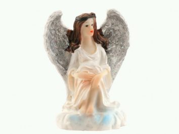 Figurka siedzącego anioła w białej sukni z brokatowymi skrzydłami na białym tle.