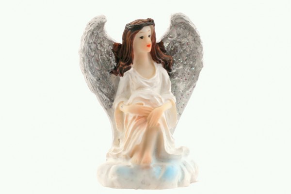 Figurka siedzącego anioła w białej sukni z brokatowymi skrzydłami na białym tle.