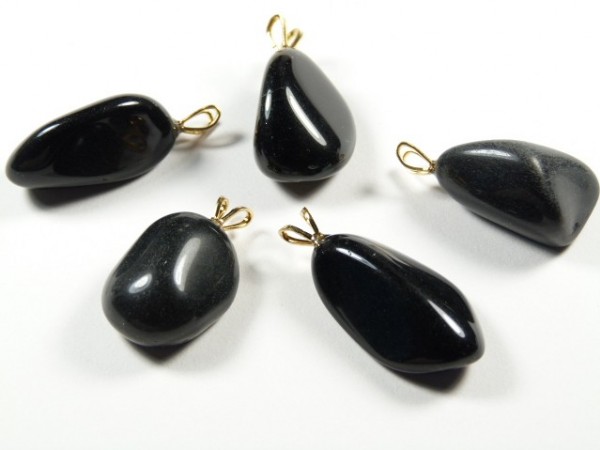 Pięć czarnych, gładkich kamieni z zawieszkami na bia­łym tle, przeznaczonych na naszyjniki.