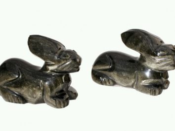 Dwa rzeźbione z kamienia zające leżące obok siebie na jasnym tle.