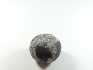 Okrągły kamień o czarno-białym wzorze leży na białym tle.