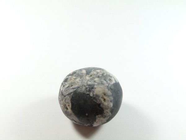 Okrągły kamień o czarno-białym wzorze leży na białym tle.