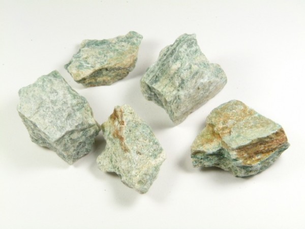 Serpentynit - kamień naturalny, surowy, nieszlifowany. Pięć kawałków zielonkawego minerału leży na białym tle.