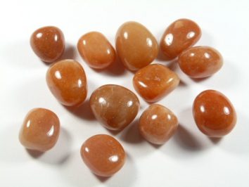 Polerowane kamienie awenturynu pomarańczowego leżące na białym tle.