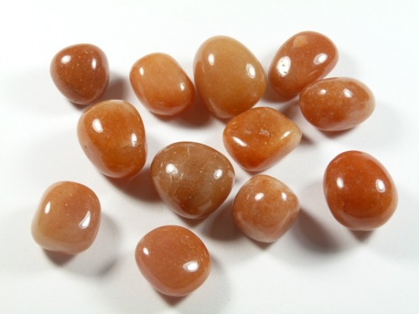 Polerowane kamienie awenturynu pomarańczowego leżące na białym tle.