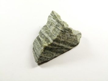 Szaro-zielony kawałek skały z wyraźnymi, równoległymi pasami na jasnym tle.