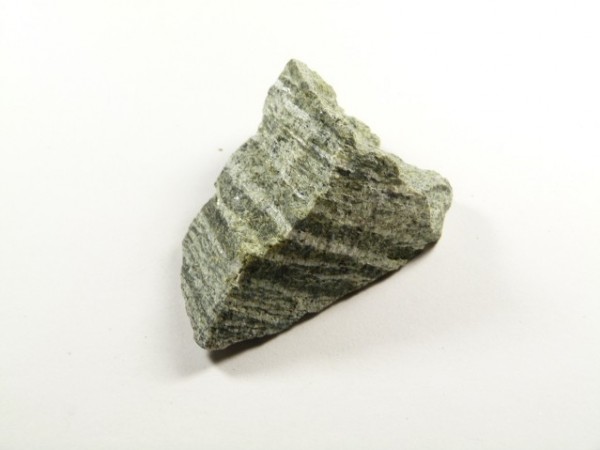 Szaro-zielony kawałek skały z wyraźnymi, równoległymi pasami na jasnym tle.