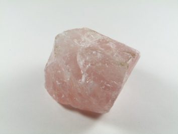 Różowy, surowy kryształ kwarcu leży na białym tle.