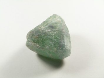 Zielony, surowy kamień leży na białym tle.