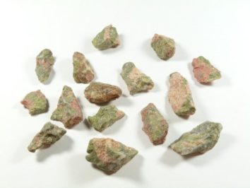 Kilka surowych, zielono-różowych kamieni ułożonych na białym tle.