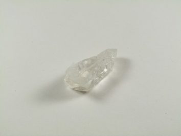 Przezroczysty kryształ kwarcu leży na białym tle.