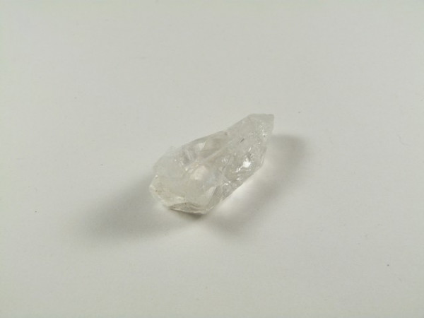 Przezroczysty kryształ kwarcu leży na białym tle.