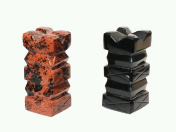 Dwie pionowe figurki szachowe z kamienia: jedna czerwona, druga czarna, na jasnym tle.