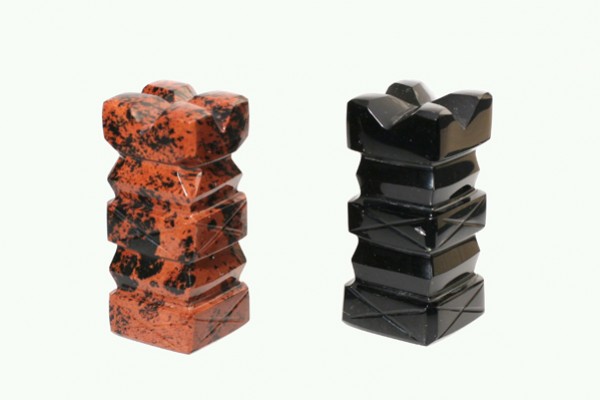 Dwie pionowe figurki szachowe z kamienia: jedna czerwona, druga czarna, na jasnym tle.