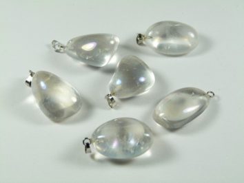 Sześć przezroczystych kamieni z zawieszkami leży na białym tle.