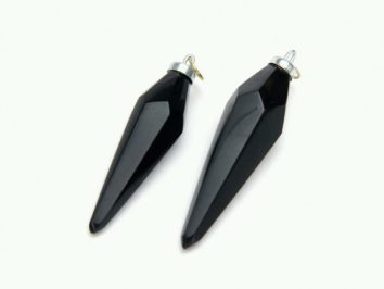 Dwa czarne, fasetowane wisiorki w kształcie szpiców leżące na białym tle.