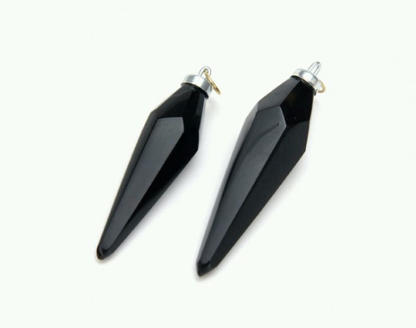 Dwa czarne, fasetowane wisiorki w kształcie szpiców leżące na białym tle.