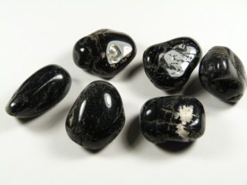 Sześć wypolerowanych, czarnych kamieni z białymi żyłkami leży na białym tle.