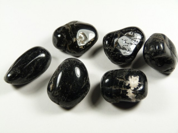 Sześć wypolerowanych, czarnych kamieni z białymi żyłkami leży na białym tle.