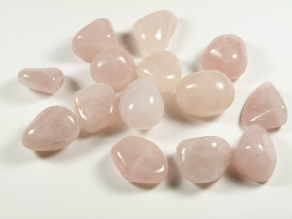 Różowy kwarc - kamień gładzony, polerowany, szlifowany i bębnowany w formie otoczaka. Kilka wypolerowanych kamieni różowego kwarcu leży na białym tle.