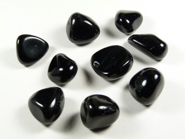 Obsydian czarny - kamień gładzony, polerowany, szlifowany i bębnowany w formie otoczaka. Dziewięć czarnych, gładkich kamieni leży na białym tle.