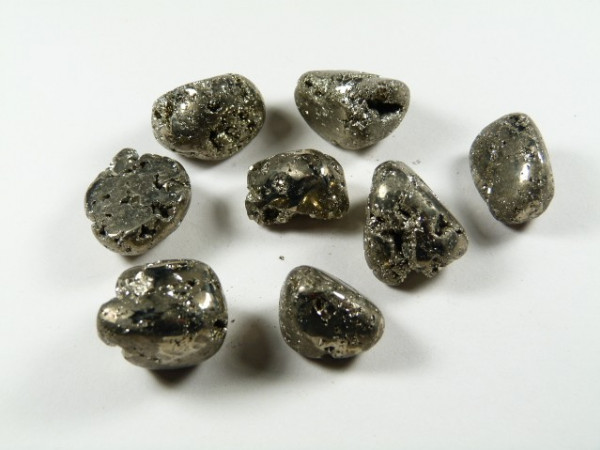 Piryt - kamień gładzony, polerowany, szlifowany i bębnowany w formie otoczaka. Osiem kawałków błyszczącego pirytu leży na białym tle.