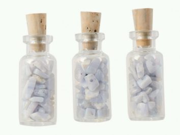 Trzy szklane butelki z korkiem wypełnione drobnymi, jasnymi kamykami.