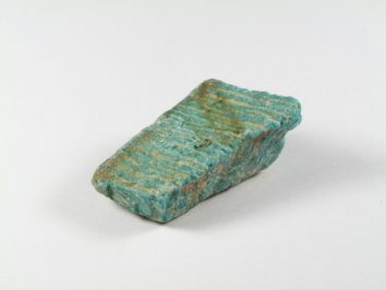 Amazonit - kamień naturalny, surowy, nieszlifowany. Niebiesko-zielony minerał amazonit o nieregularnym kształcie, leżący na białym tle.