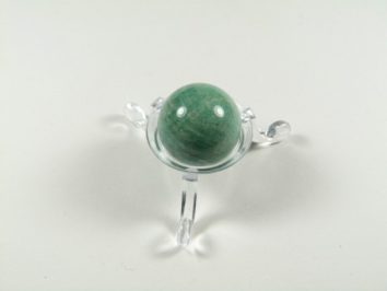 Zielona kula z kamienia na przezroczystej podstawce, ustawiona na jasnym tle.