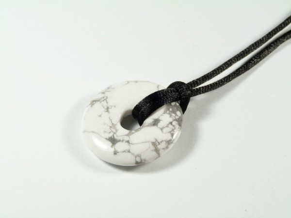 Biały okrągły wisiorek z czarnym sznurkiem, wykonany z kamienia z szarymi żyłkami.