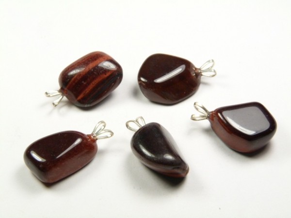 Pięć brązowych, wypolerowanych kamieni z zawieszkami na białym tle.