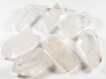 Siedem przezroczystych kryształów kwarcu leży na białej powierzchni.