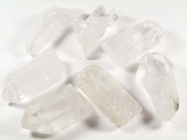 Siedem przezroczystych kryształów kwarcu leży na białej powierzchni.
