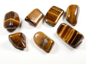 Siedem polerowanych kamieni tygrysiego oka ułożonych na białym tle.