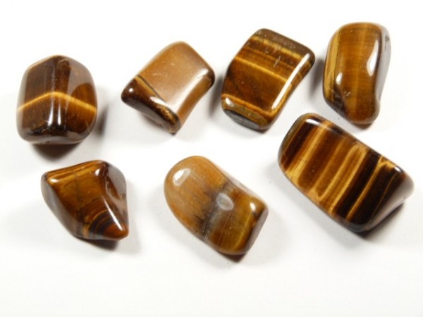 Siedem polerowanych kamieni tygrysiego oka ułożonych na białym tle.