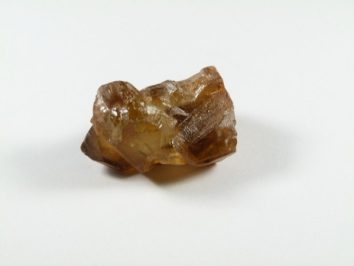 Cytryn naturalny - kamień naturalny surowy nieszlifowany. Brązowy, nieoszlifowany kryształ leży na białym tle.