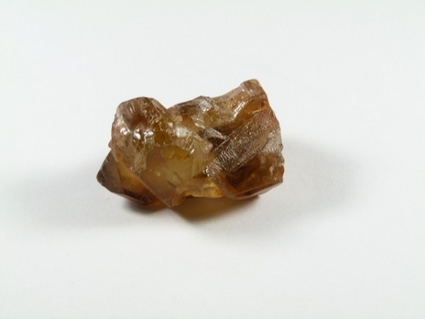 Cytryn naturalny - kamień naturalny surowy nieszlifowany. Brązowy, nieoszlifowany kryształ leży na białym tle.