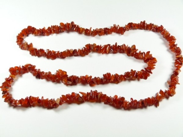 Naszyjnik z czerwonych, nieregularnych kamieni ułożony na białym tle.