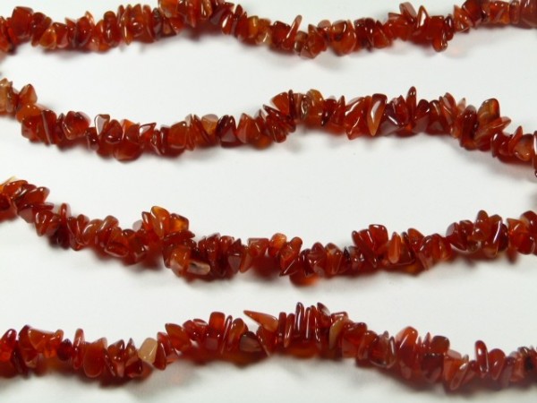 Czerwone korale z nieoszlifowanych kamieni ułożone w kilku rzędach na białym tle.