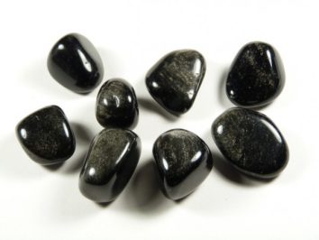 Obsydian srebrny - kamień gładzony, polerowany, szlifowany i bębnowany w formie otoczaka. Osiem wypolerowanych, czarnych kamieni leży na białym tle.