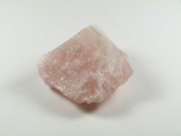 Różowy, nieoszlifowany kryształ kwarcu leży na białym tle.