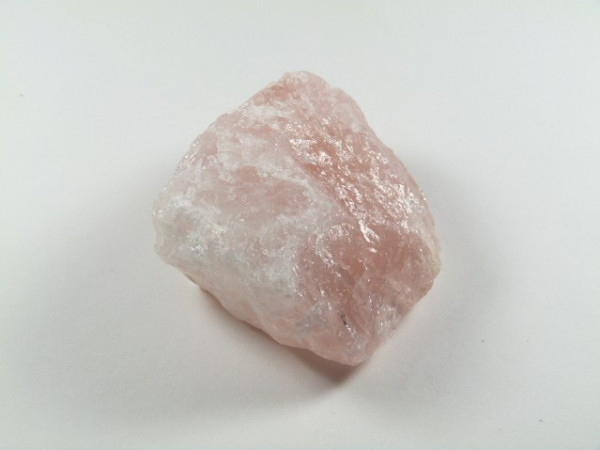 Różowy, nieoszlifowany kamień kwarcu na jasnym tle.