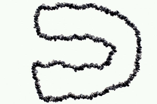 Naszyjnik z czarnych, nieregularnych kamieni ułożony w kształt litery „D” na jasnym tle.