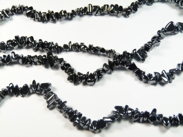 Czarne naszyjniki z drobnych kamieni hematytu ułożone na białym tle.