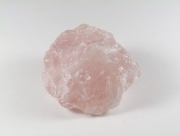 Różowy, surowy kryształ kwarcu na białym tle.