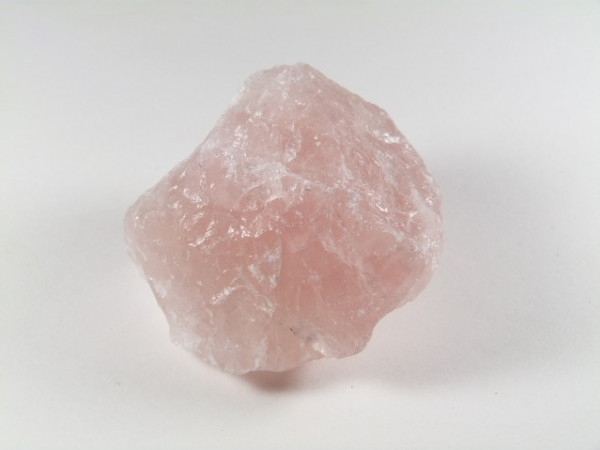 Różowy, surowy kryształ kwarcu leży na białym tle.